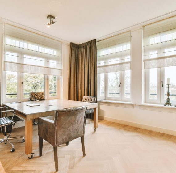 a home office area with wood flooring and large windows that look out onto the street in front of the house