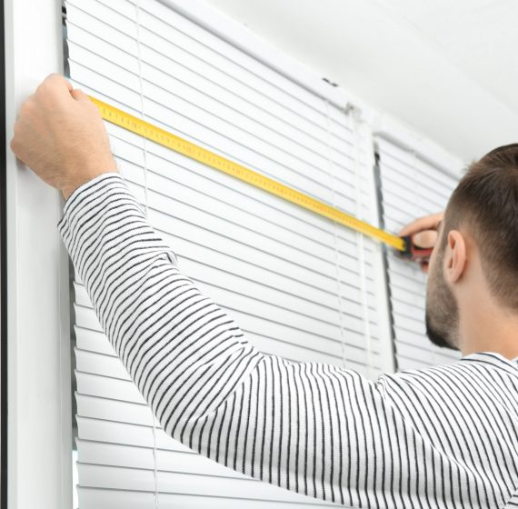 Young man installing window shades at home